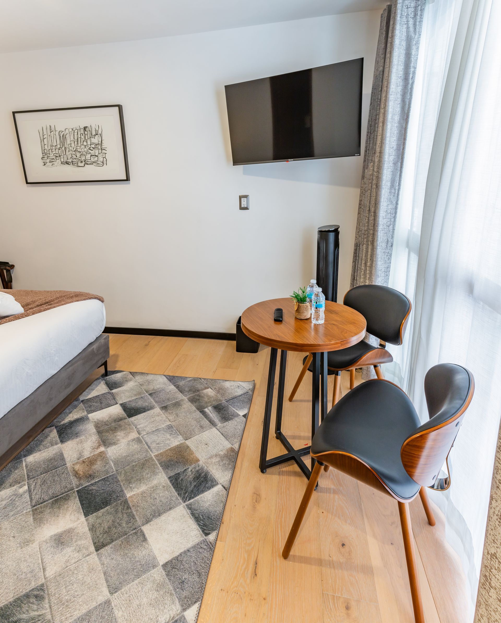 Un dormitorio con una cama, sillas, una mesa y un televisor de pantalla plana.
