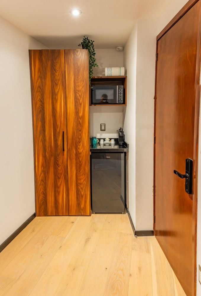 Una habitación con una puerta de madera, un armario de madera, un microondas y un refrigerador.