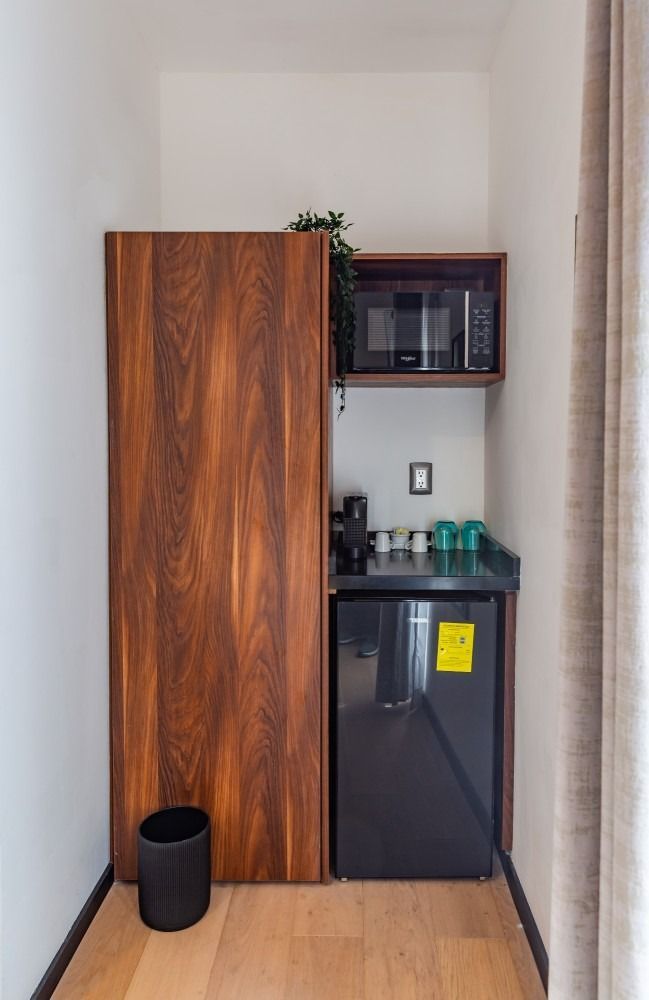 Una pequeña cocina con refrigerador, microondas y bote de basura.