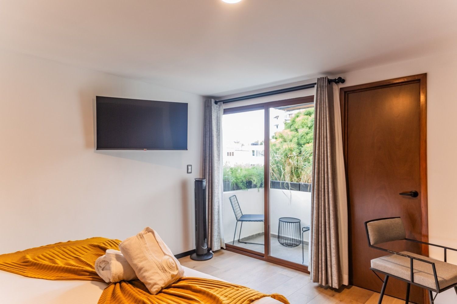 Un dormitorio con cama, silla, televisión y puertas corredizas de vidrio.