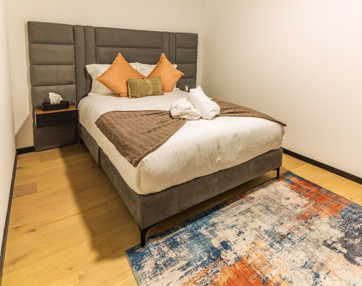 Un dormitorio con cama, alfombra y mesita de noche.