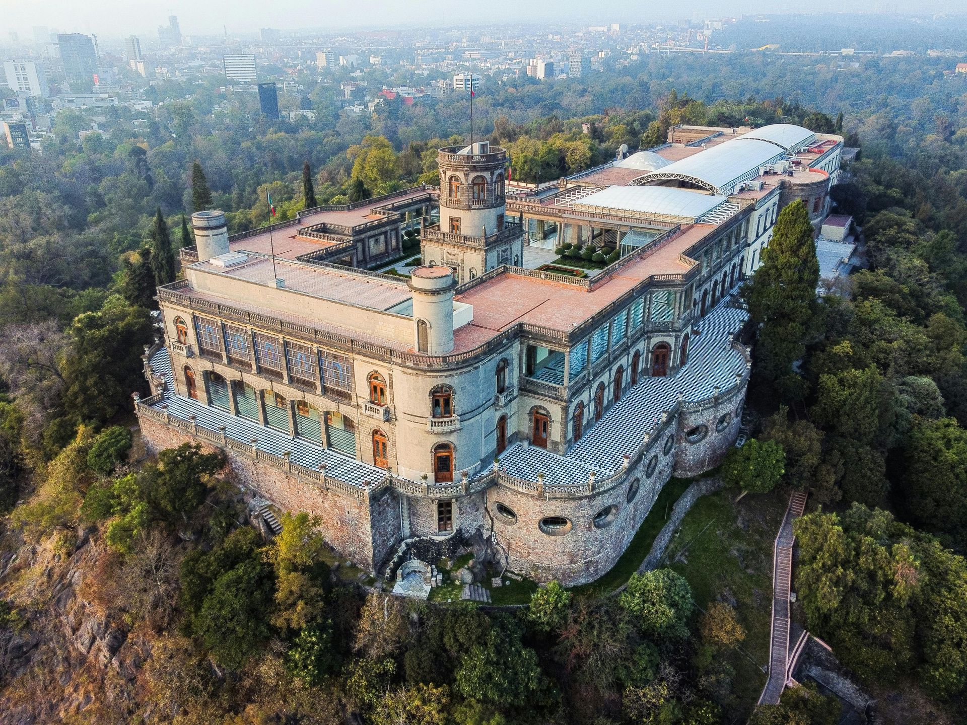 Una vista aérea de un gran edificio en la cima de una colina rodeado de árboles.
