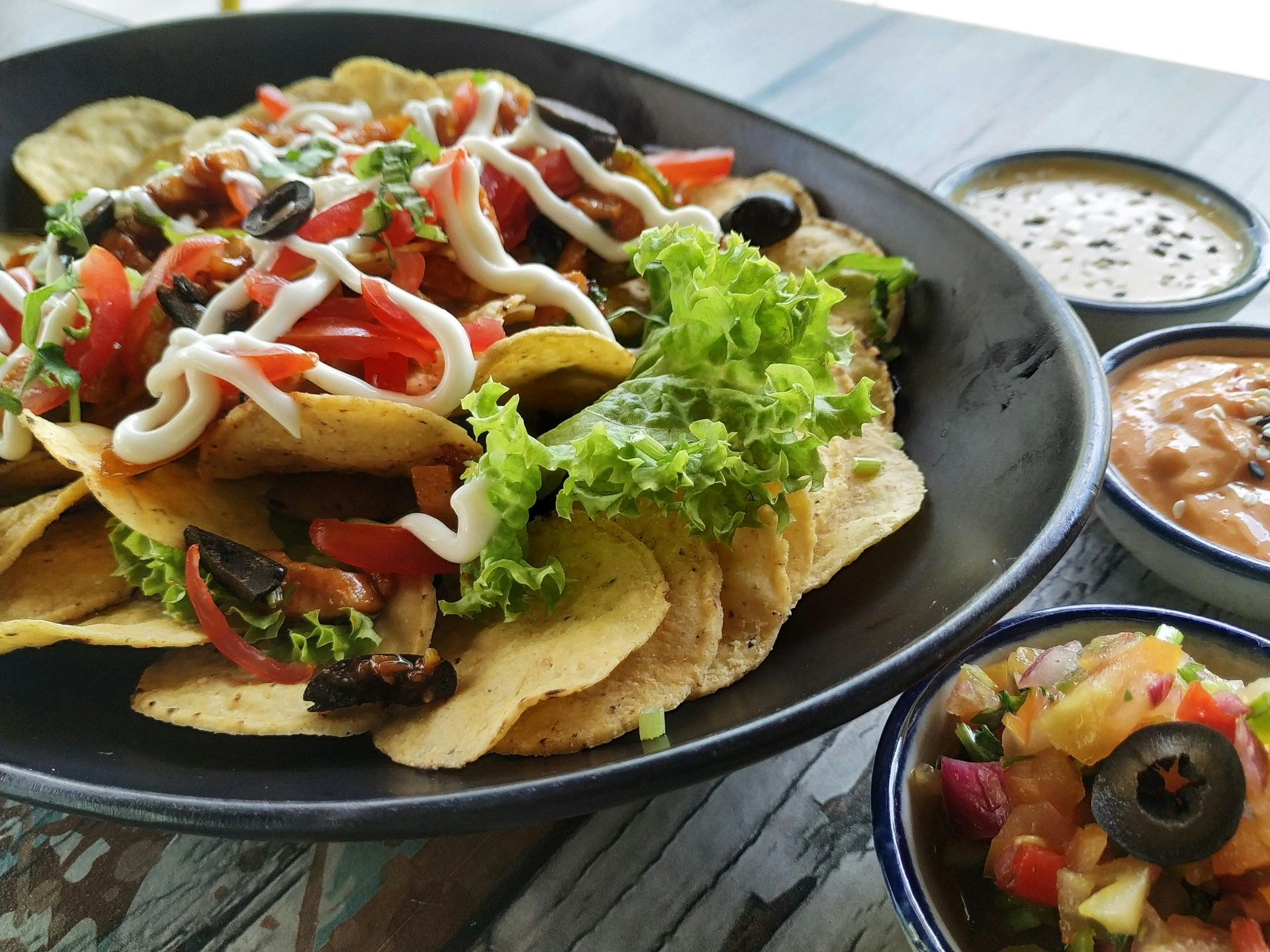 Un plato negro cubierto con nachos y salsa sobre una mesa de madera.