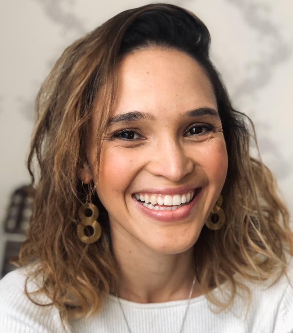 A woman wearing a white shirt and gold earrings is smiling for the camera.