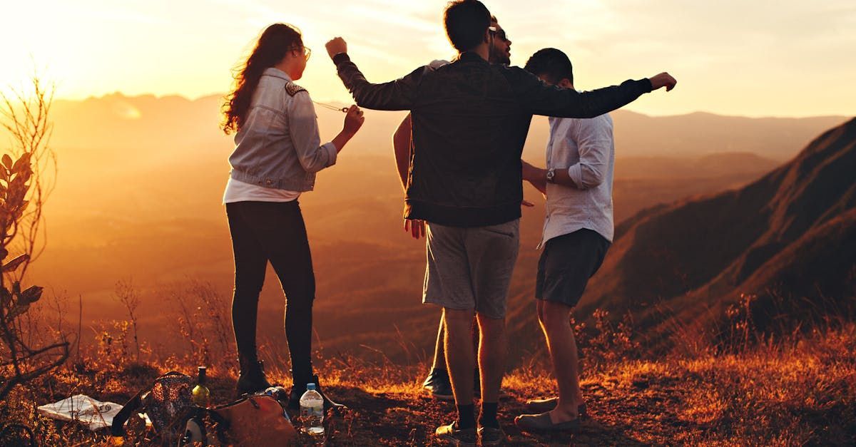 A group of people are standing on top of a hill at sunset.