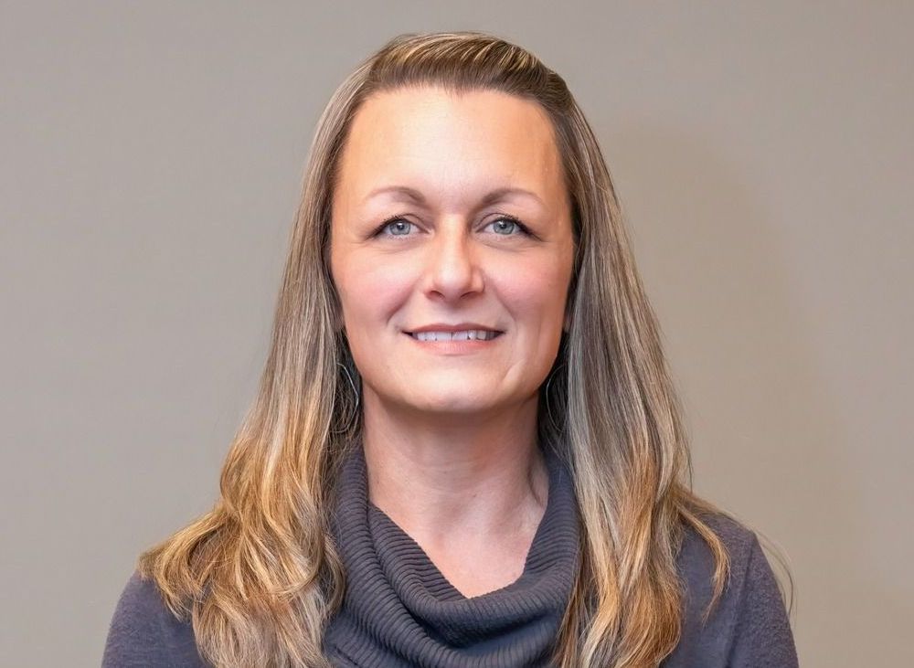 Smiling person in a gray scarf against a plain beige background