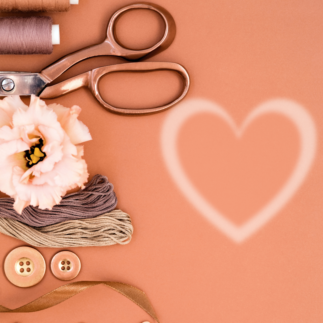 Crafting supplies and scissors on peach background with a white heart outline