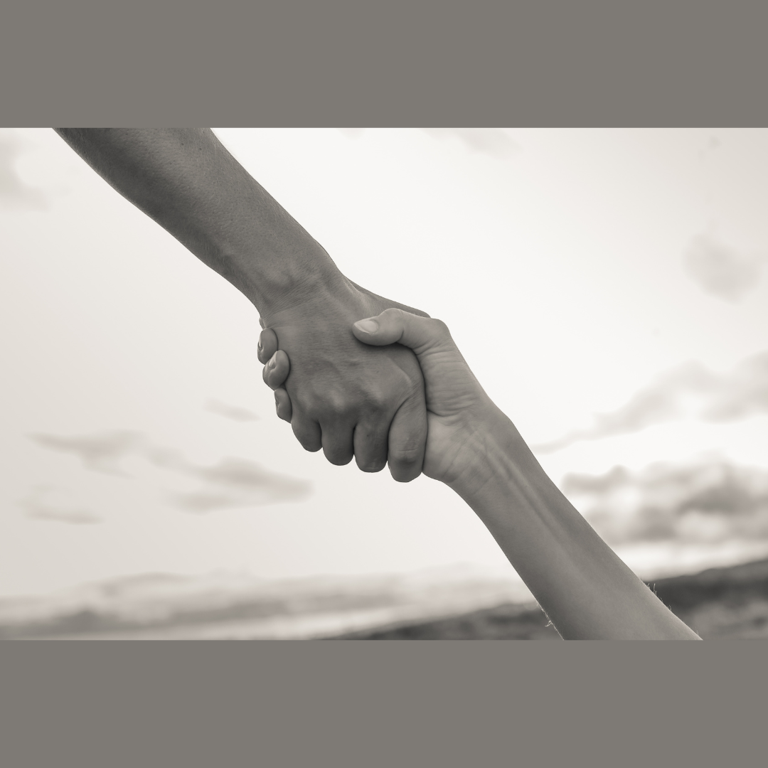 Two hands clasped in a helping grip against a blurred outdoor sky background