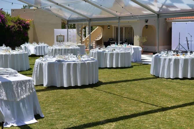 Outdoor wedding reception setup under a clear tent with round white-clothed tables on a lawn.