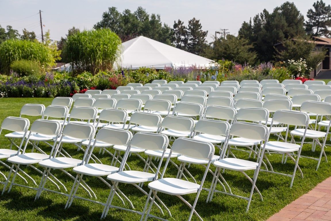 Rows of white folding chairs set up on a grassy lawn for an outdoor event, with a white tent in the background