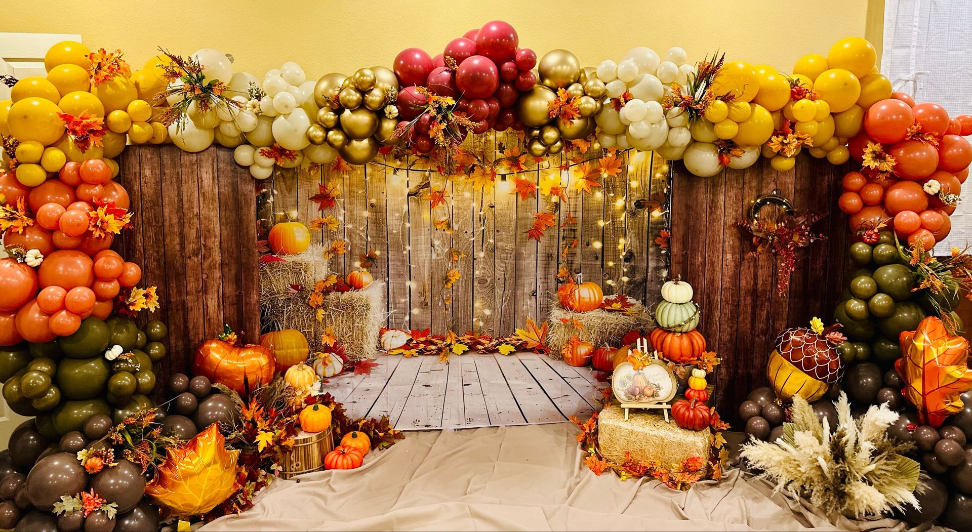 A room decorated with balloons , pumpkins , leaves and a cake.