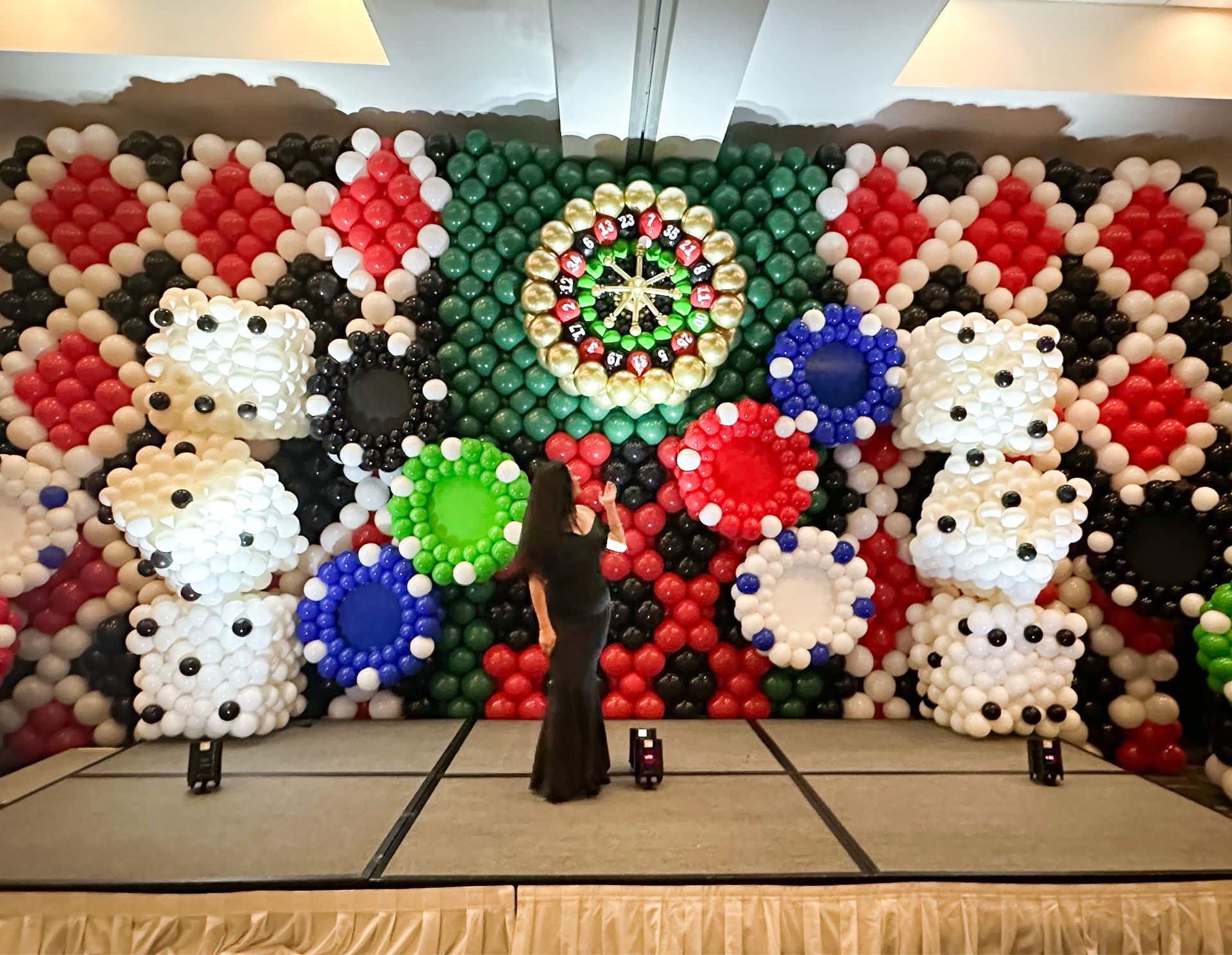 A woman is standing in front of a wall made of balloons.