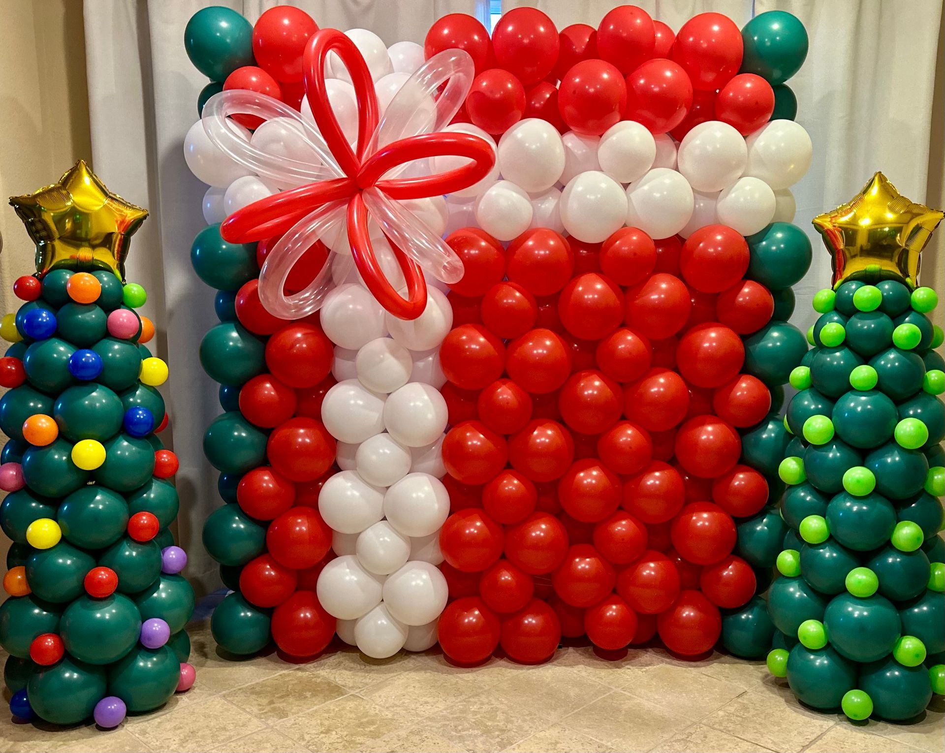 A wall of balloons decorated to look like a gift box and christmas trees.