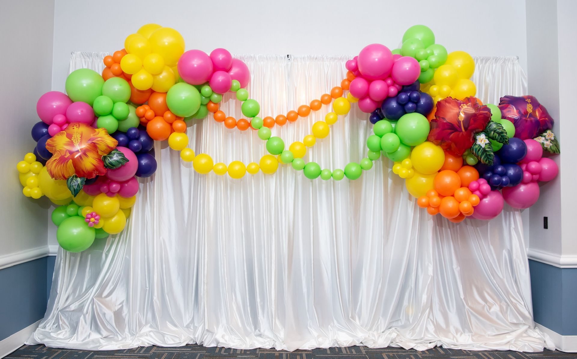 A bunch of colorful balloons are hanging on a white curtain.