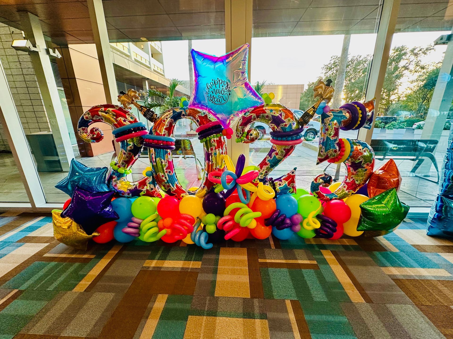 A bunch of colorful balloons are sitting on the floor in front of a window.