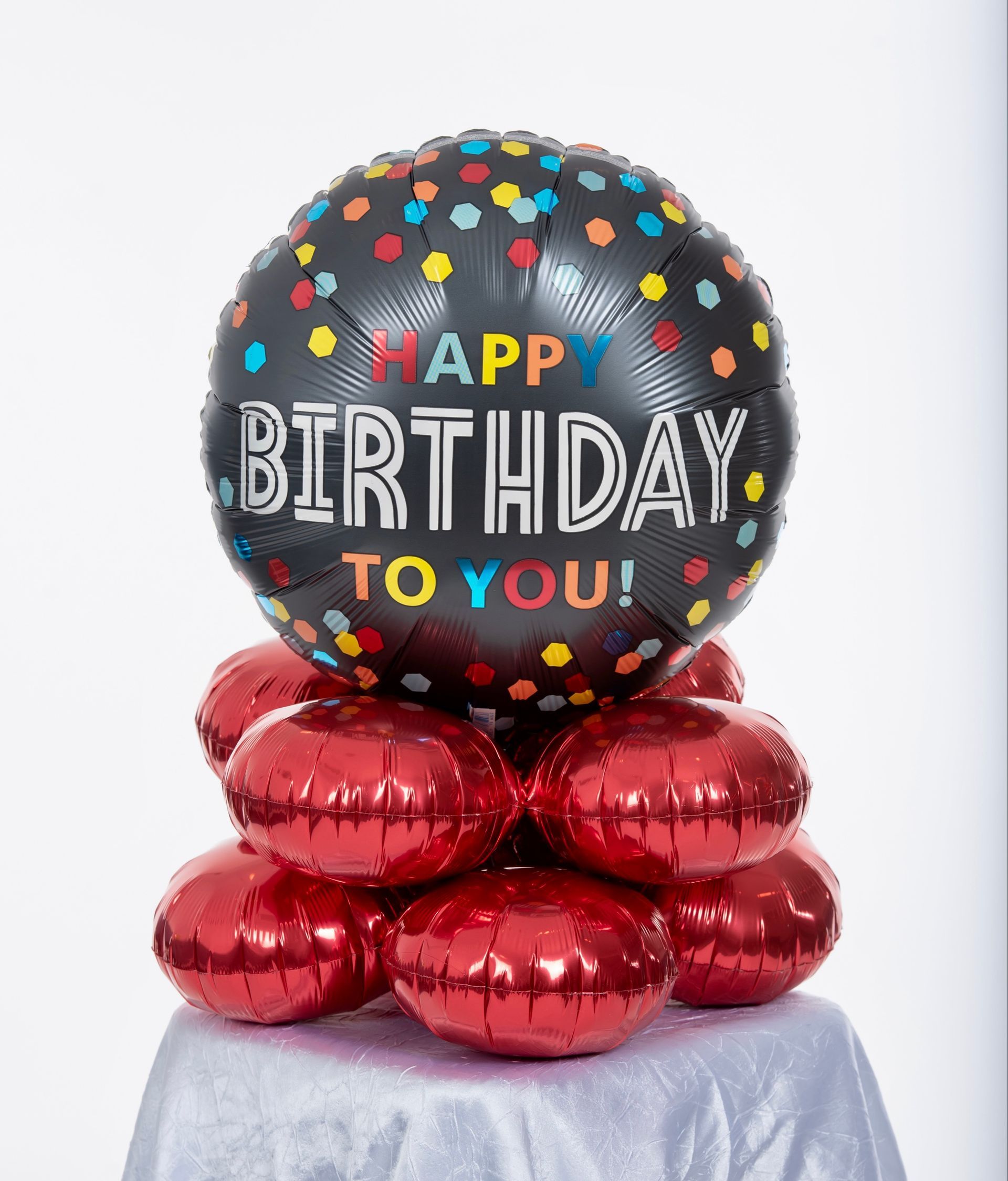 A happy birthday to you balloon is surrounded by red balloons