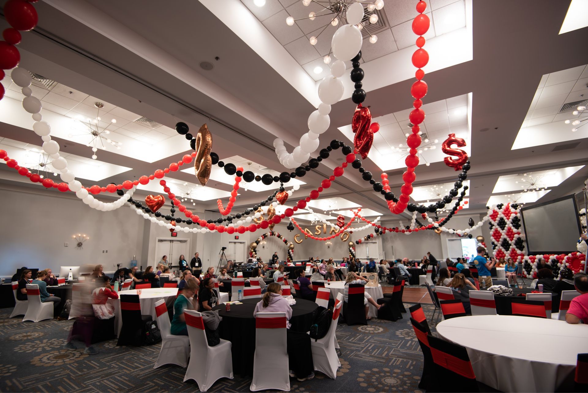 A large room with tables and chairs and balloons hanging from the ceiling