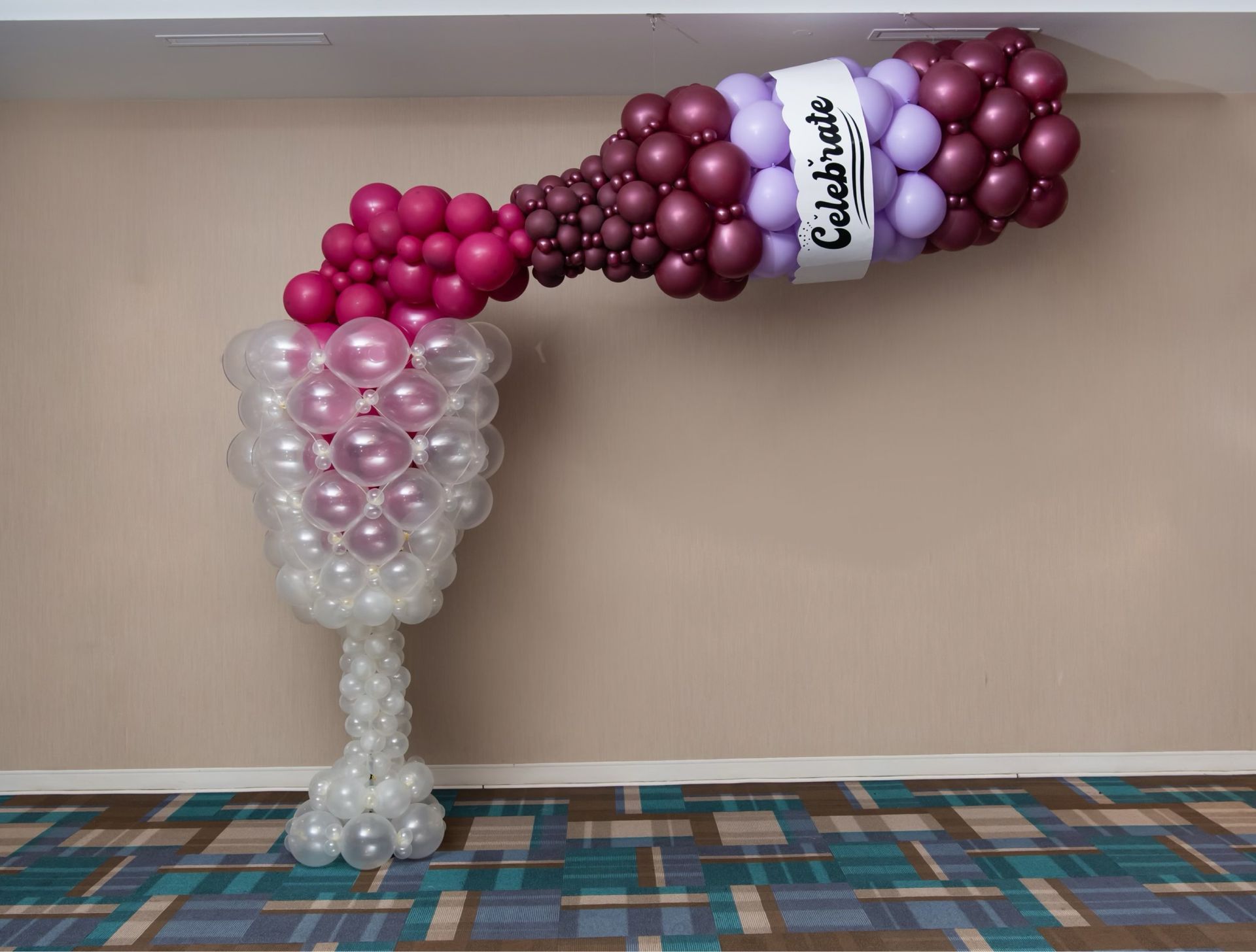A bottle of wine made out of balloons is hanging on a wall.