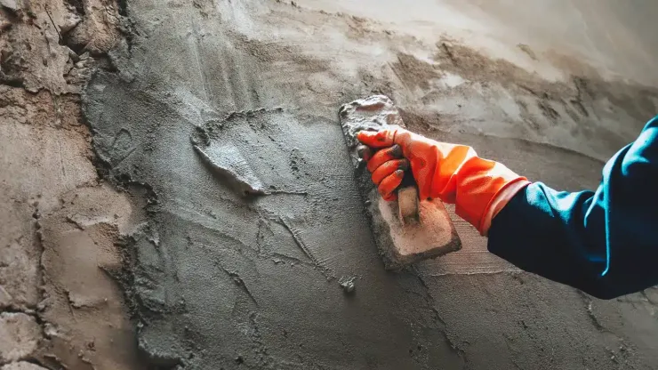 Gloved hand smoothing wet concrete on a rough concrete wall