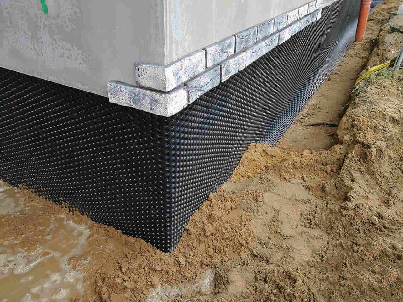 Black waterproofing mat around a house foundation corner on sandy ground