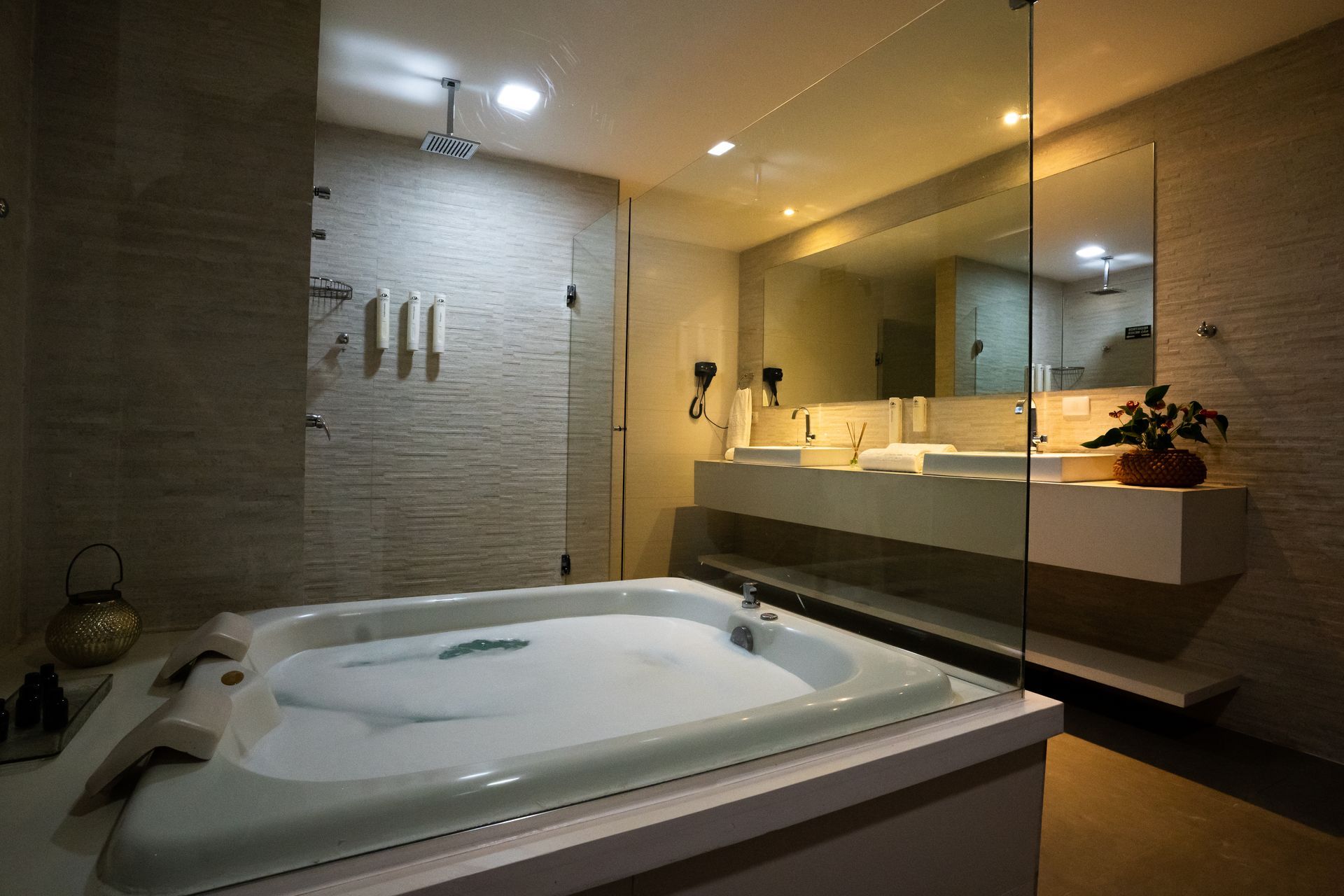 Banheiro com jacuzzi, chuveiro e um grande espelho. Tons de bege.
