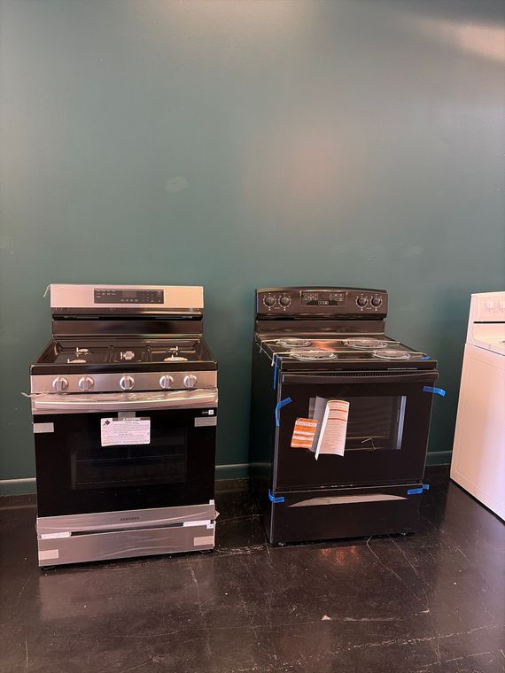 Two stoves/ovens displayed side by side against a teal wall on a store floor.