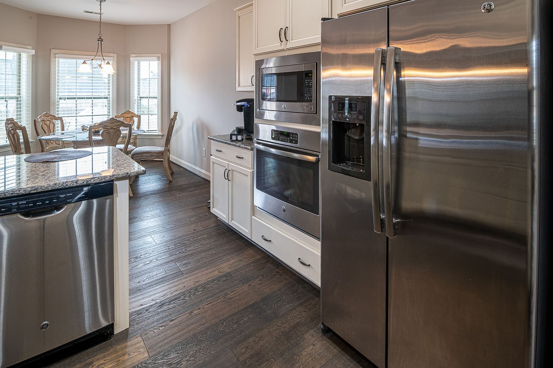 Modern kitchen with stainless steel appliances, white cabinets, and a dining area by a window.