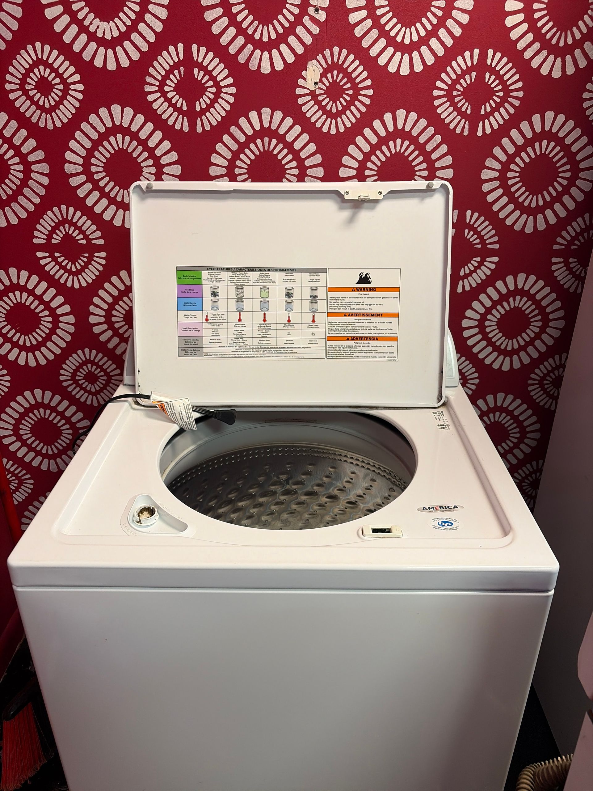 Open top-loading washing machine against red patterned wallpaper, with tub visible.