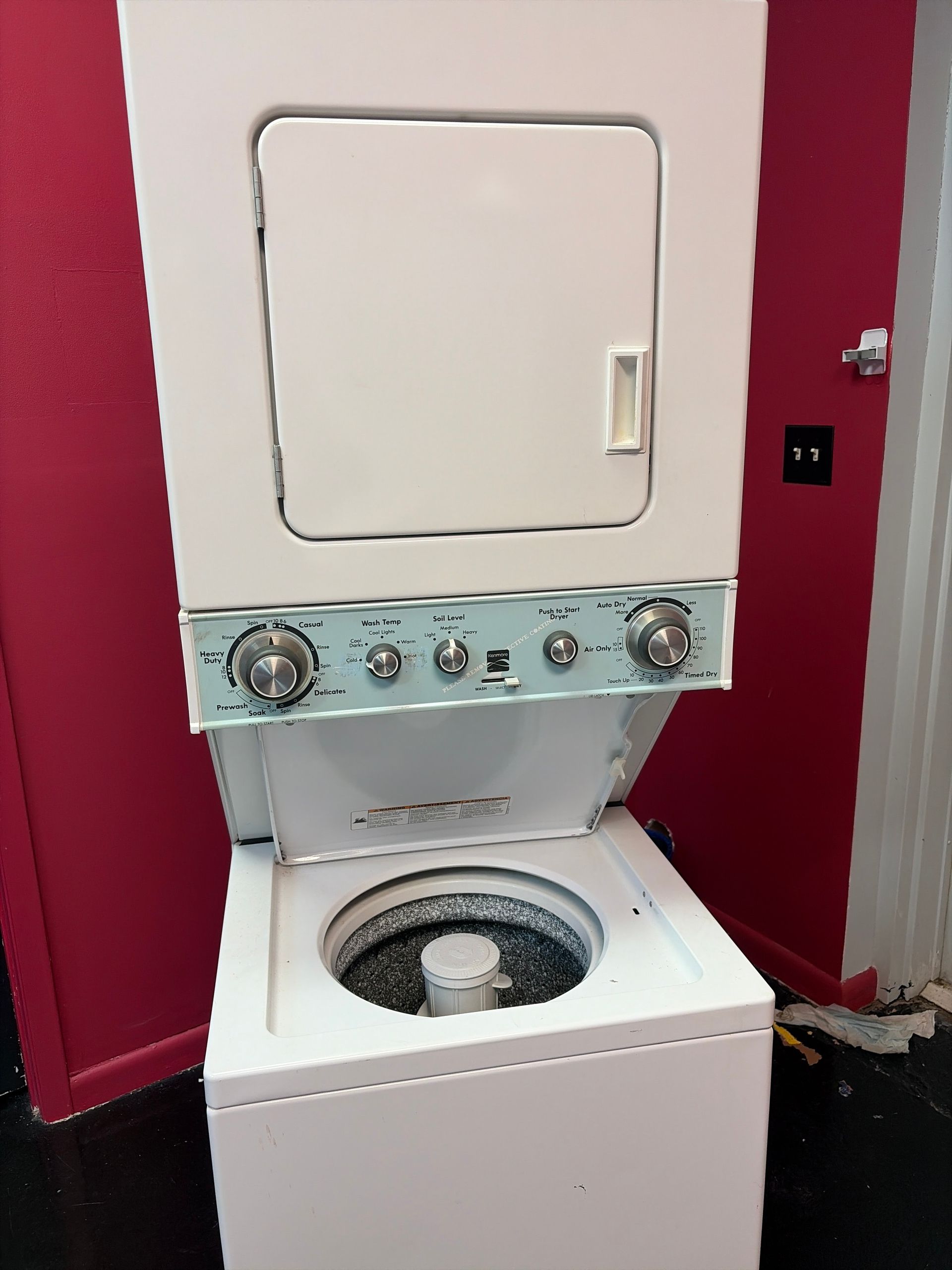 Stacked washer and dryer in a red laundry room, washer lid open.