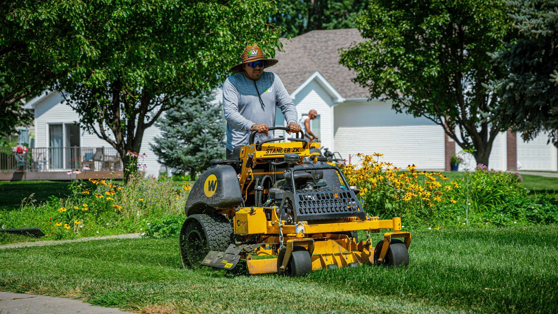 Person mowing a green lawn with a yellow riding mower in a suburban yard