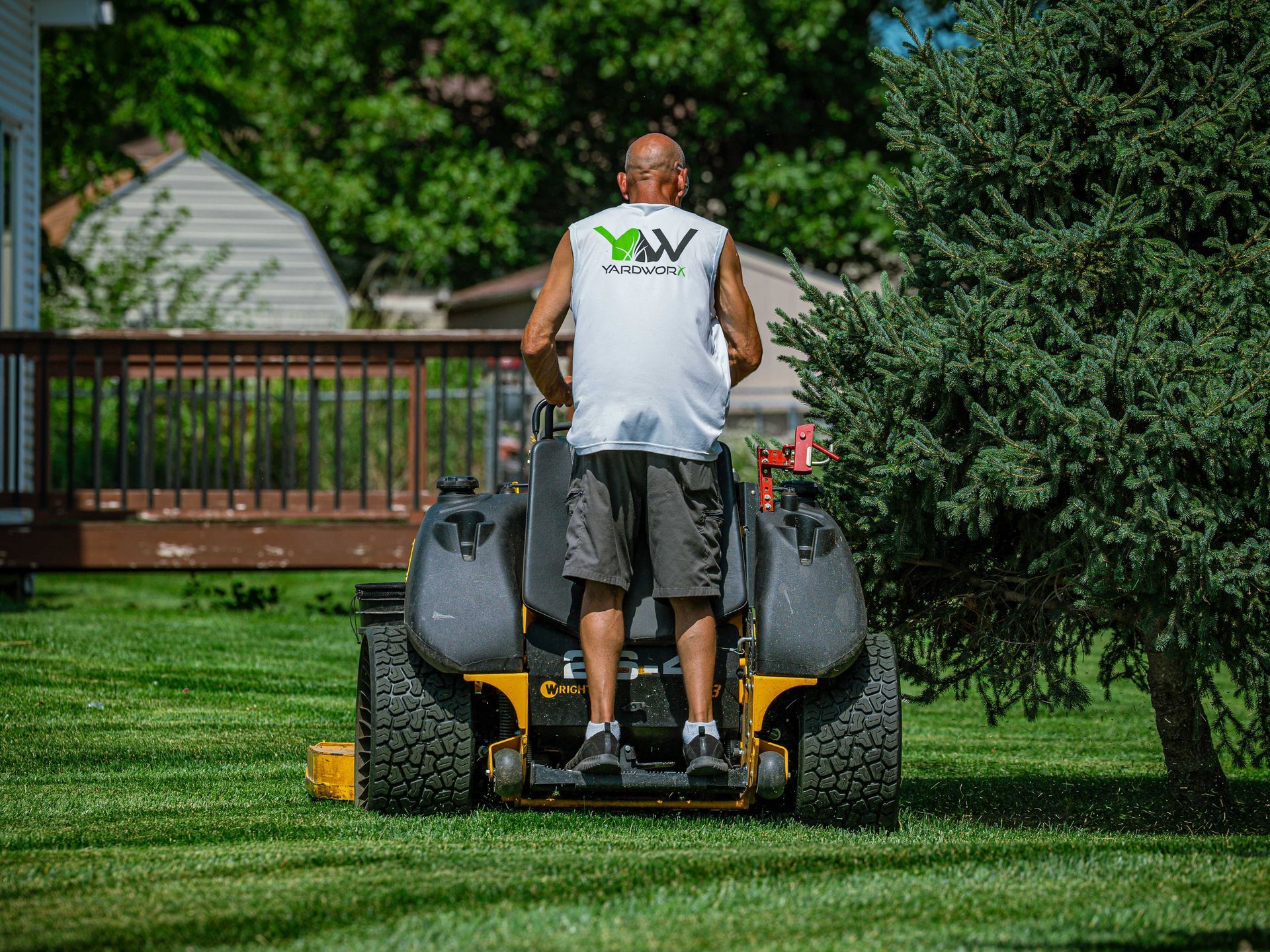 Person mowing a green lawn with a riding mower in a backyard