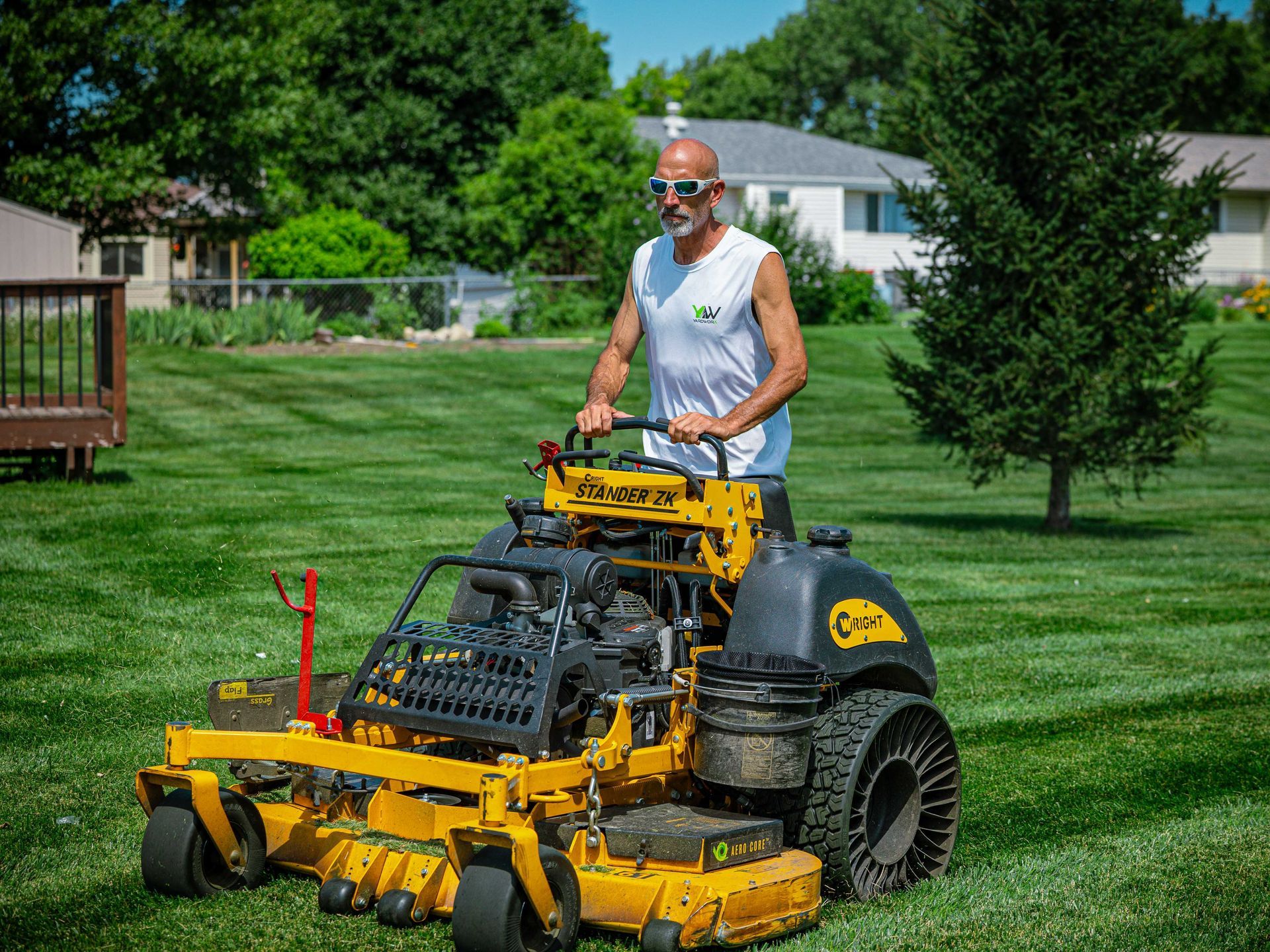Man mowing a lawn with a yellow ride-on mower in a green yard
