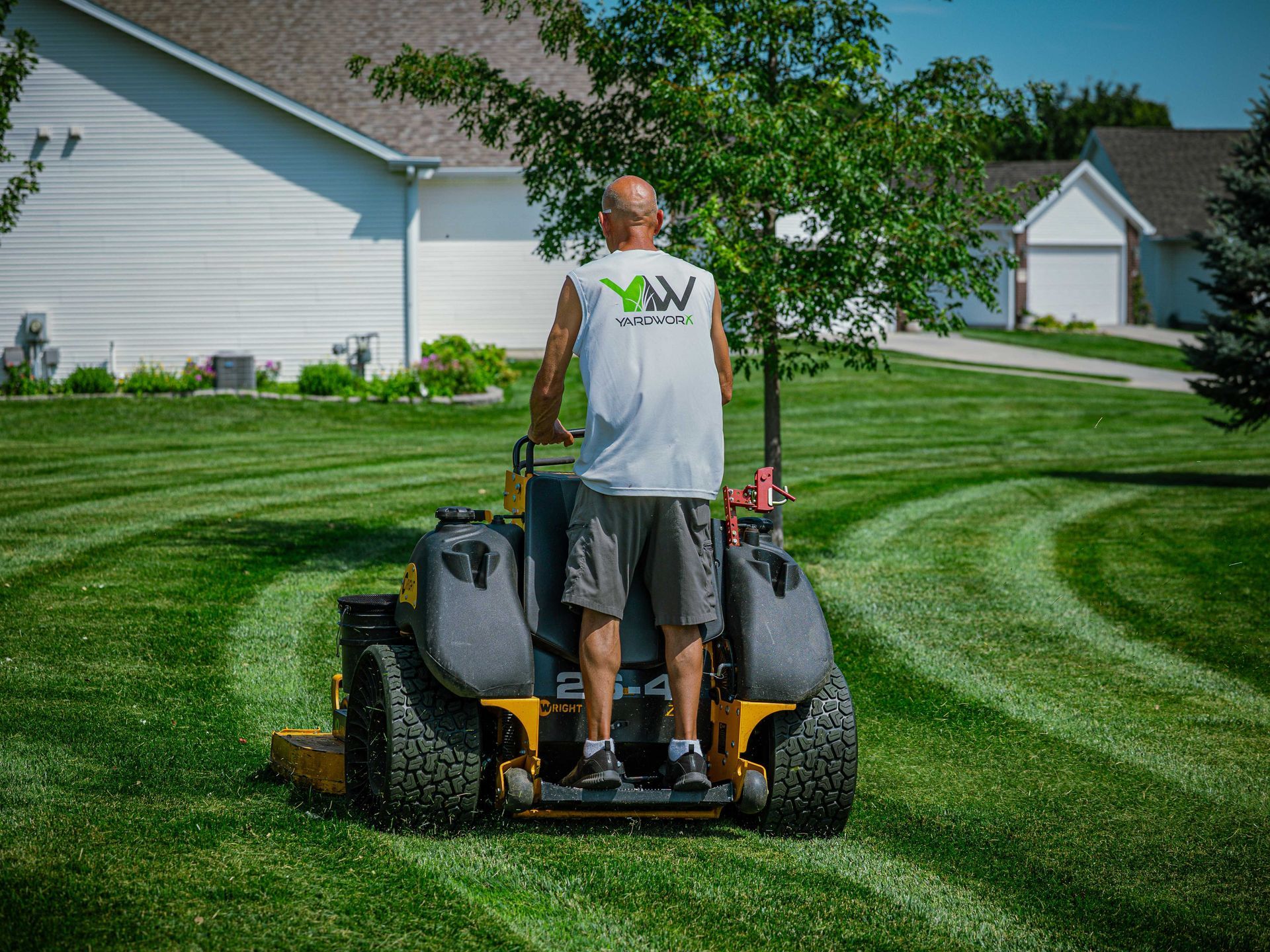 Man mowing a striped green lawn with a riding mower in a suburban yard