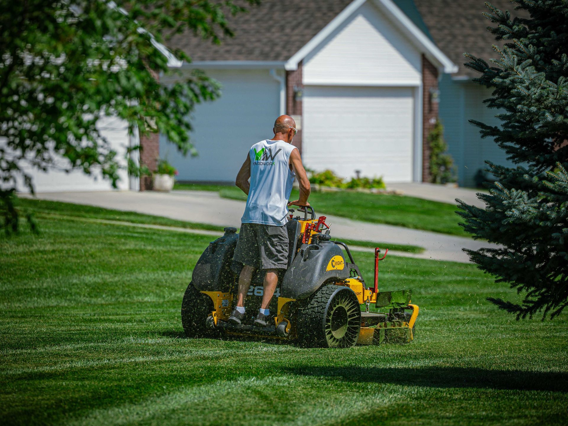 Person mowing a grassy lawn with a riding mower in a suburban yard