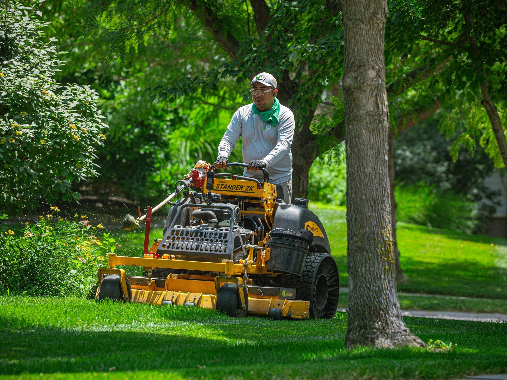 Man mowing a green lawn with a riding mower in a leafy park