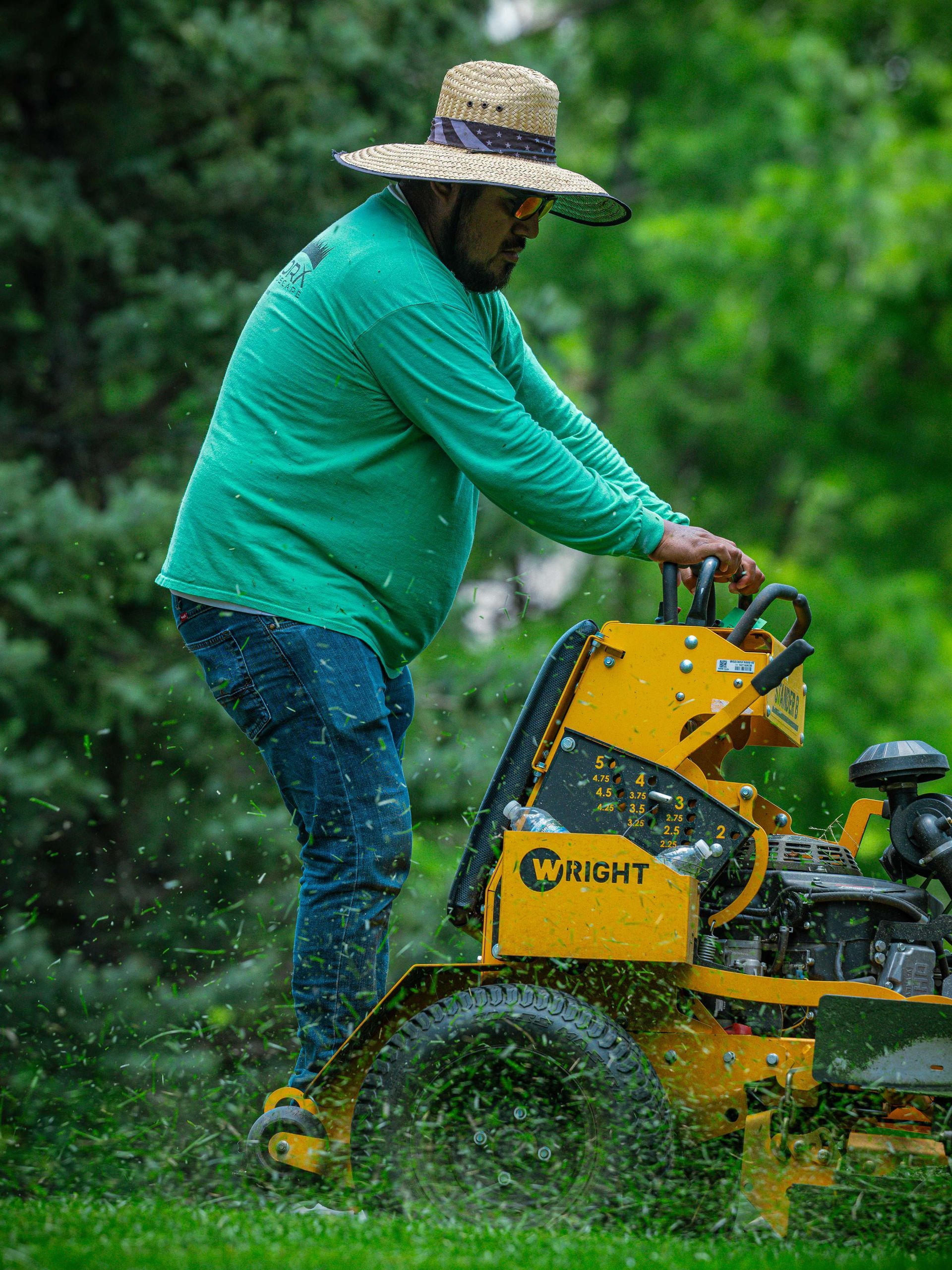 Person pushing a yellow lawn mower through wet grass in the rain, wearing a straw hat and green shirt