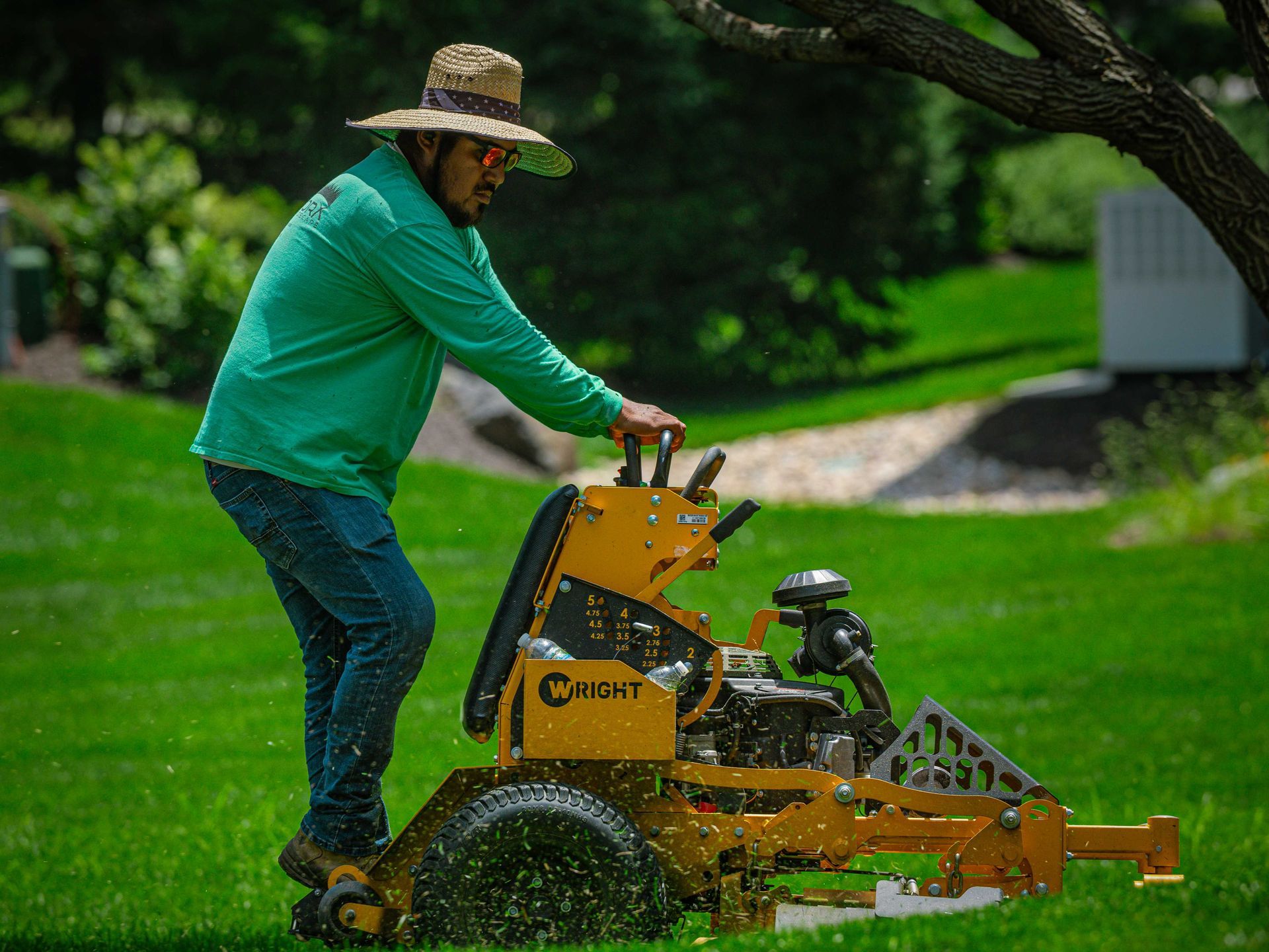 Person mowing a lawn with a yellow riding mower on a bright green yard.