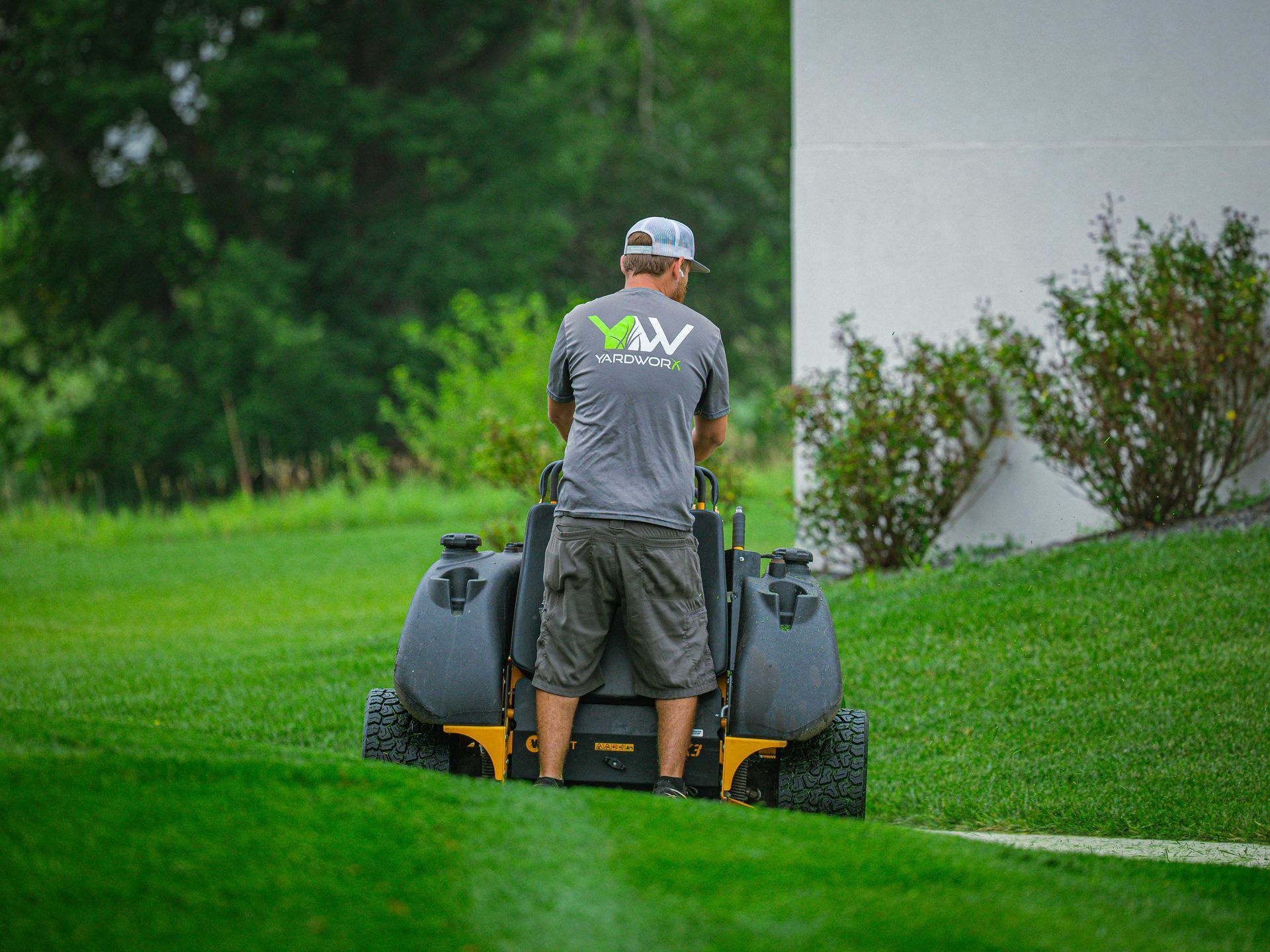 Person mowing a green lawn with a riding mower beside a building