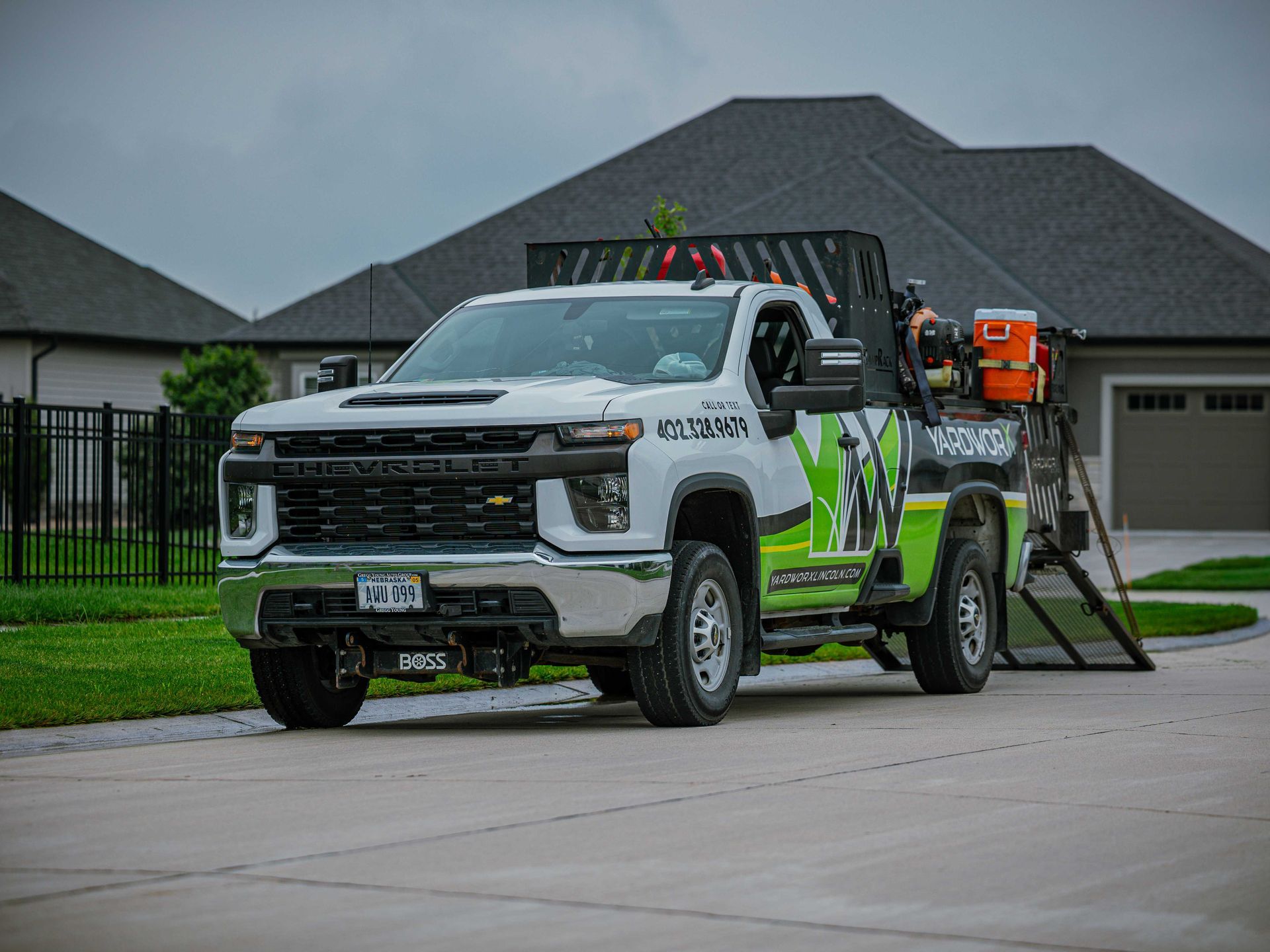 White utility truck with safety cones and equipment parked in a suburban driveway near a house.