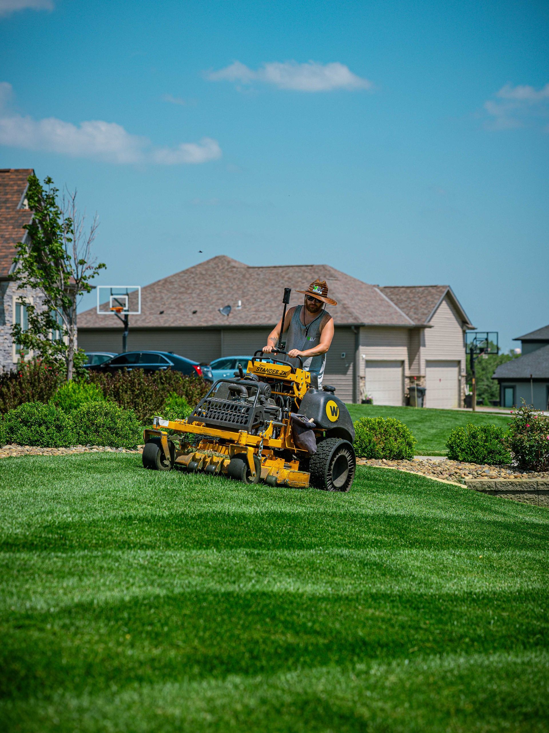Person mowing a bright green suburban lawn with a yellow riding mower on a sunny day