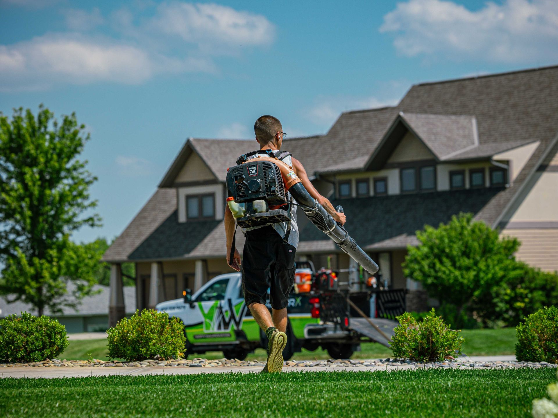 Worker using a backpack sprayer in front of a suburban house on a sunny day