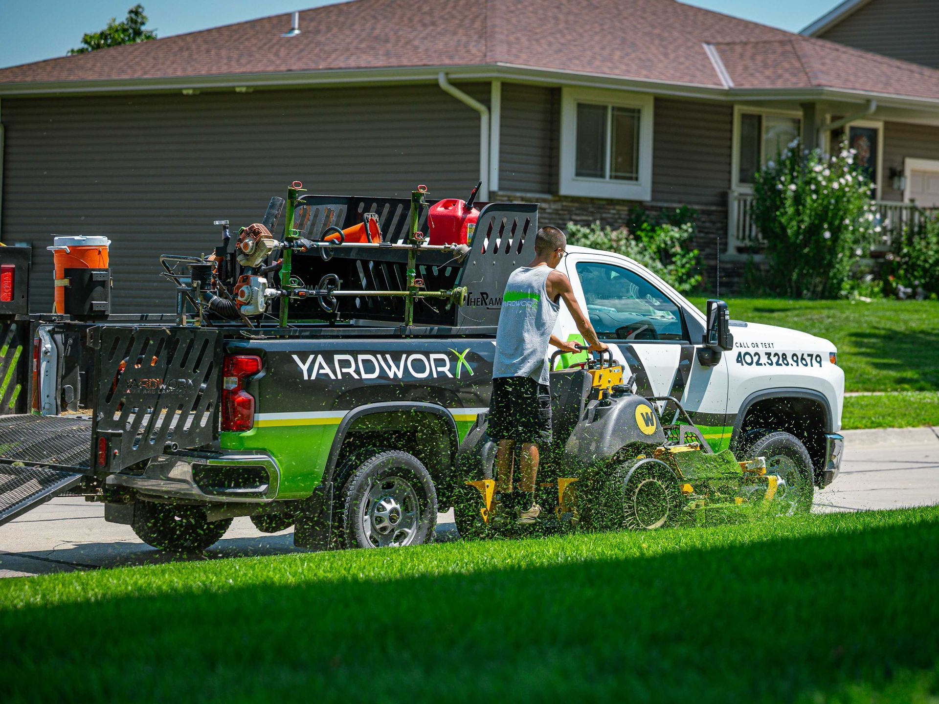 Yardwork truck with equipment parked in a suburban driveway beside a house and lawn.