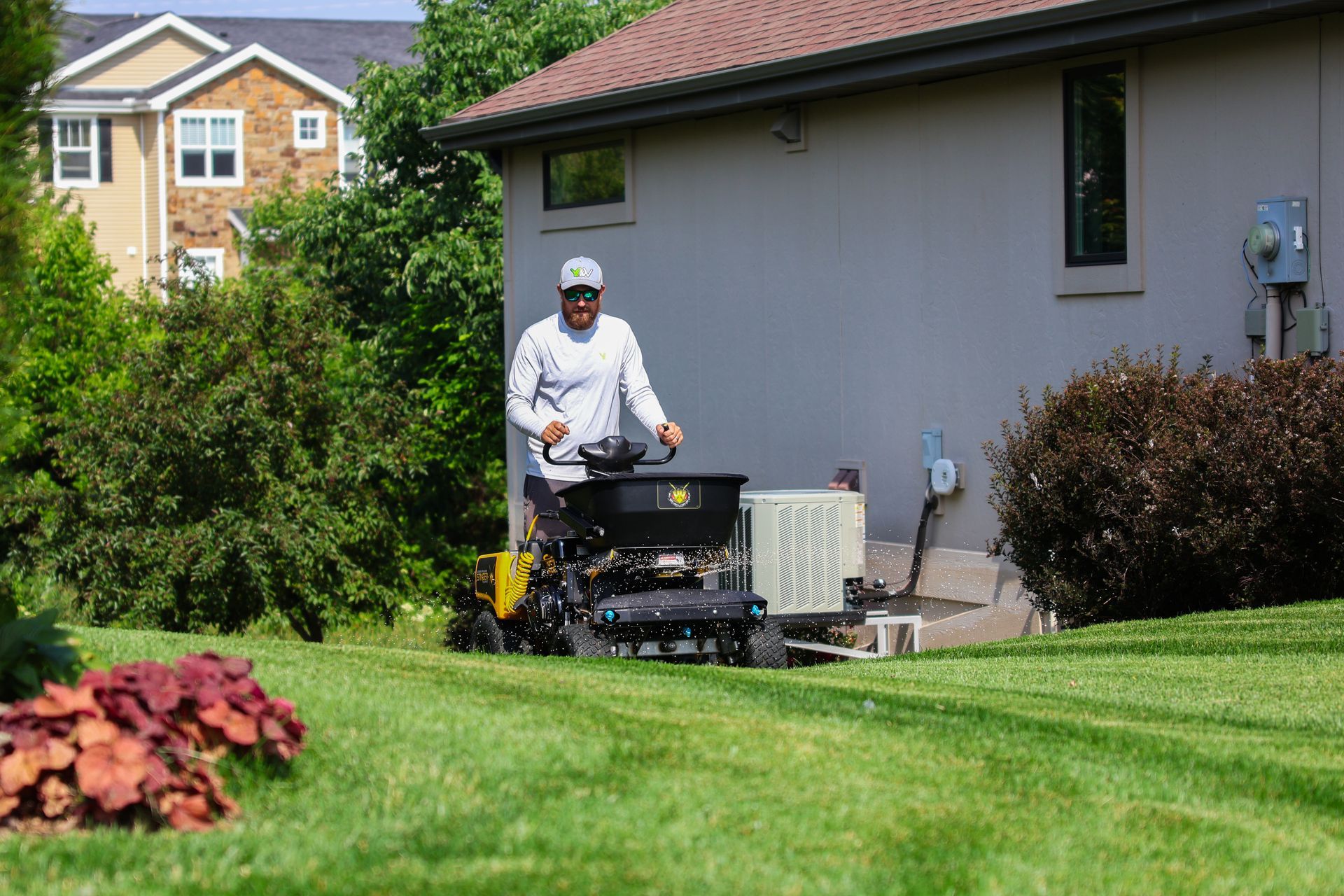 Man operating a lawn spreader on a green lawn near a house.