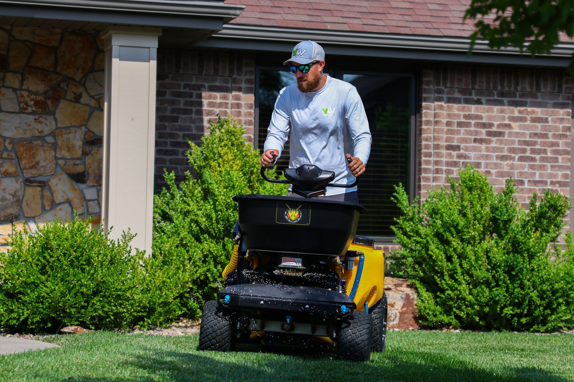 Man using a yellow lawn spreader on a green lawn in front of a house.