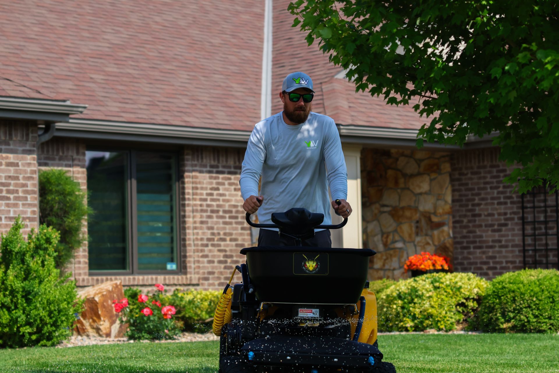 Man operating a fertilizer spreader on a lawn in front of a house.