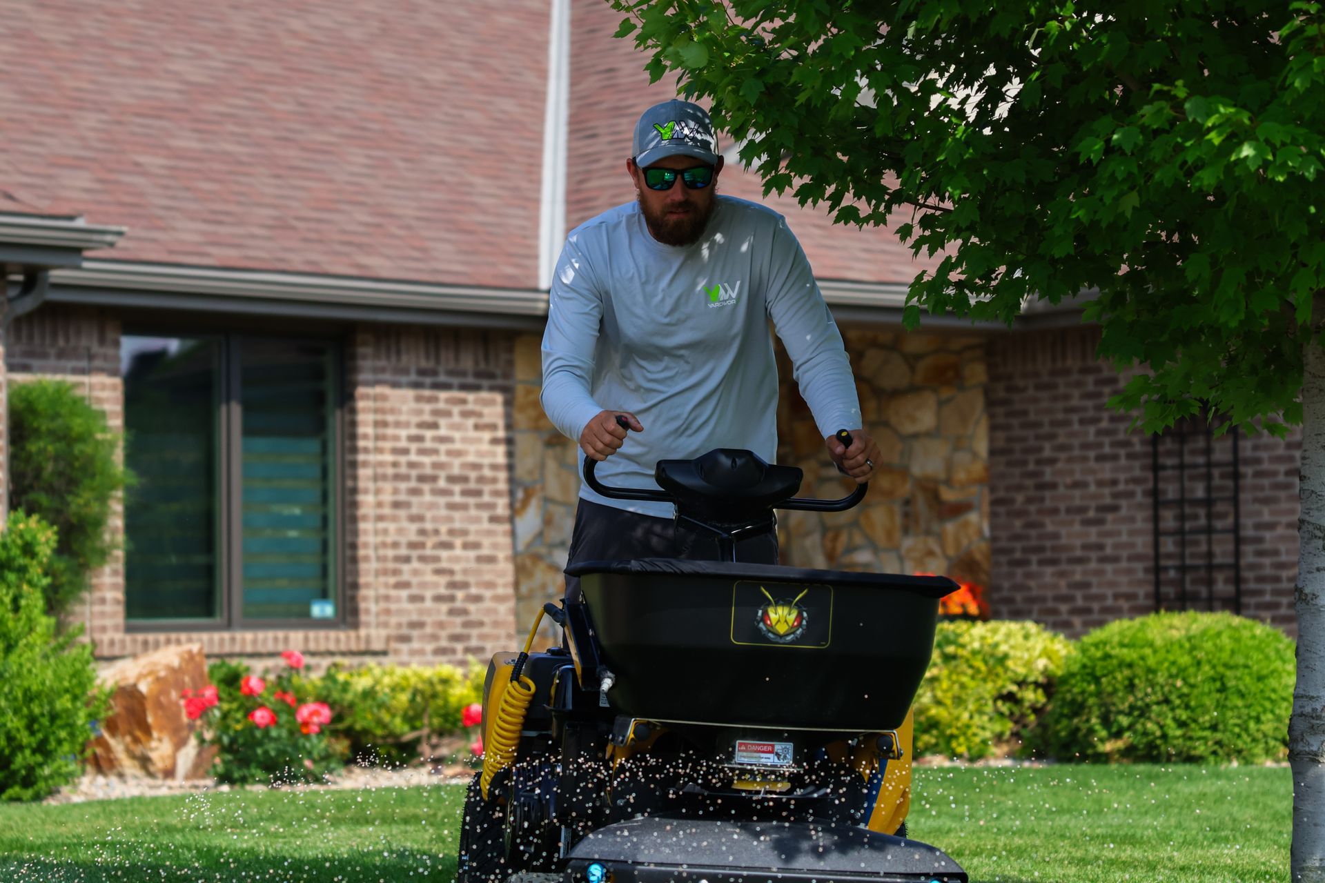 Man operating a spreader on a lawn in front of a house.