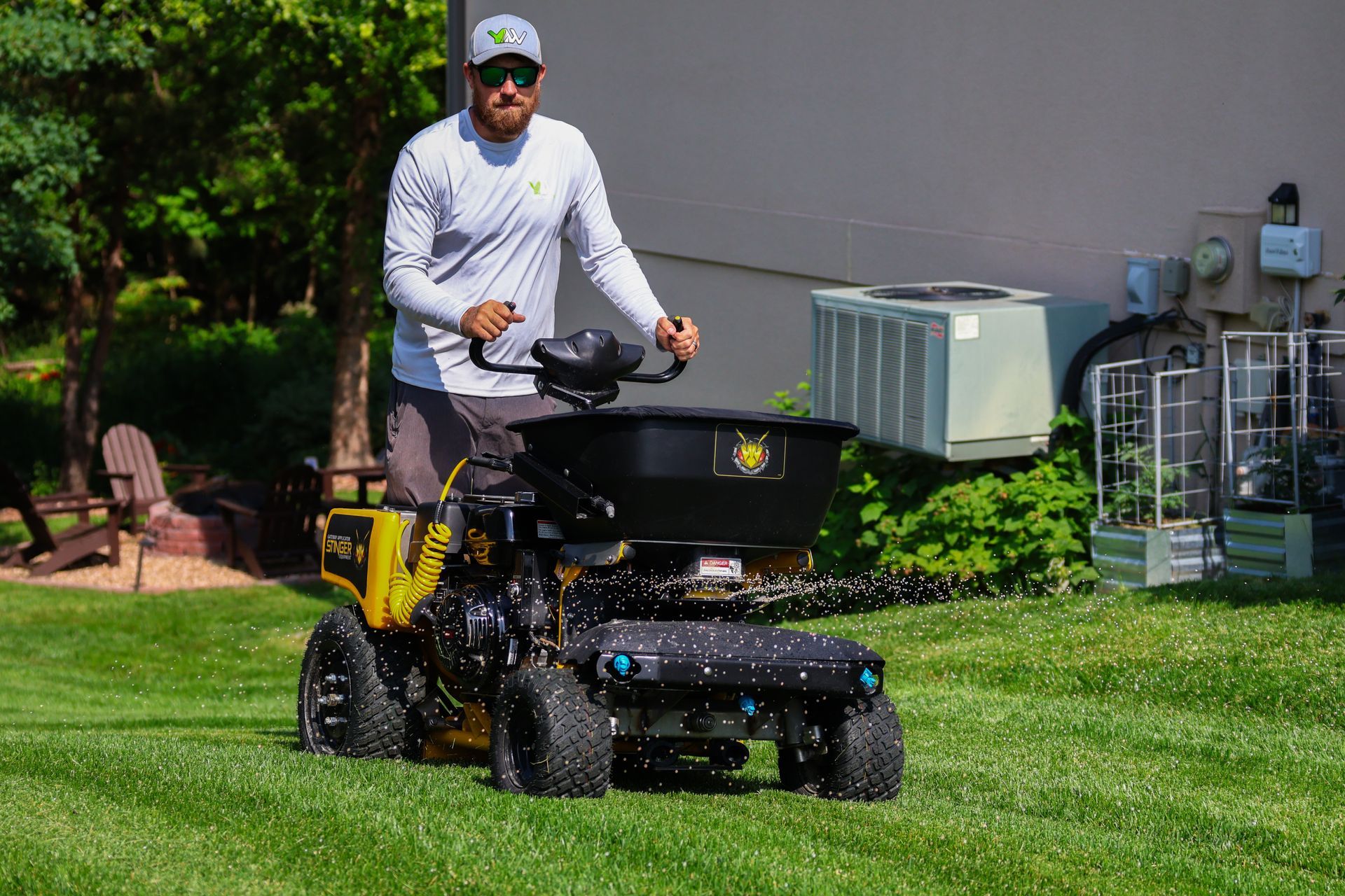 Man operating a yellow lawn spreader on a green lawn.