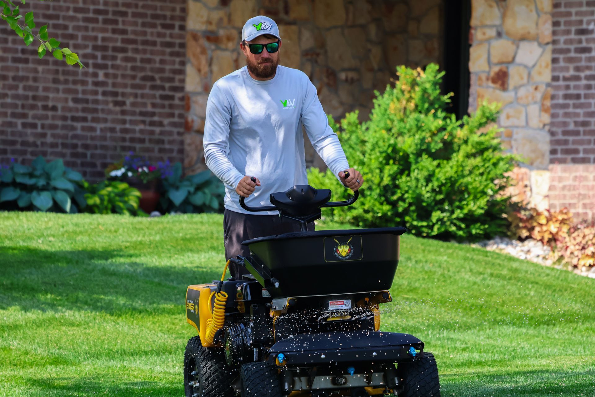 Man spreading fertilizer on lawn with a spreader, in front of a house.