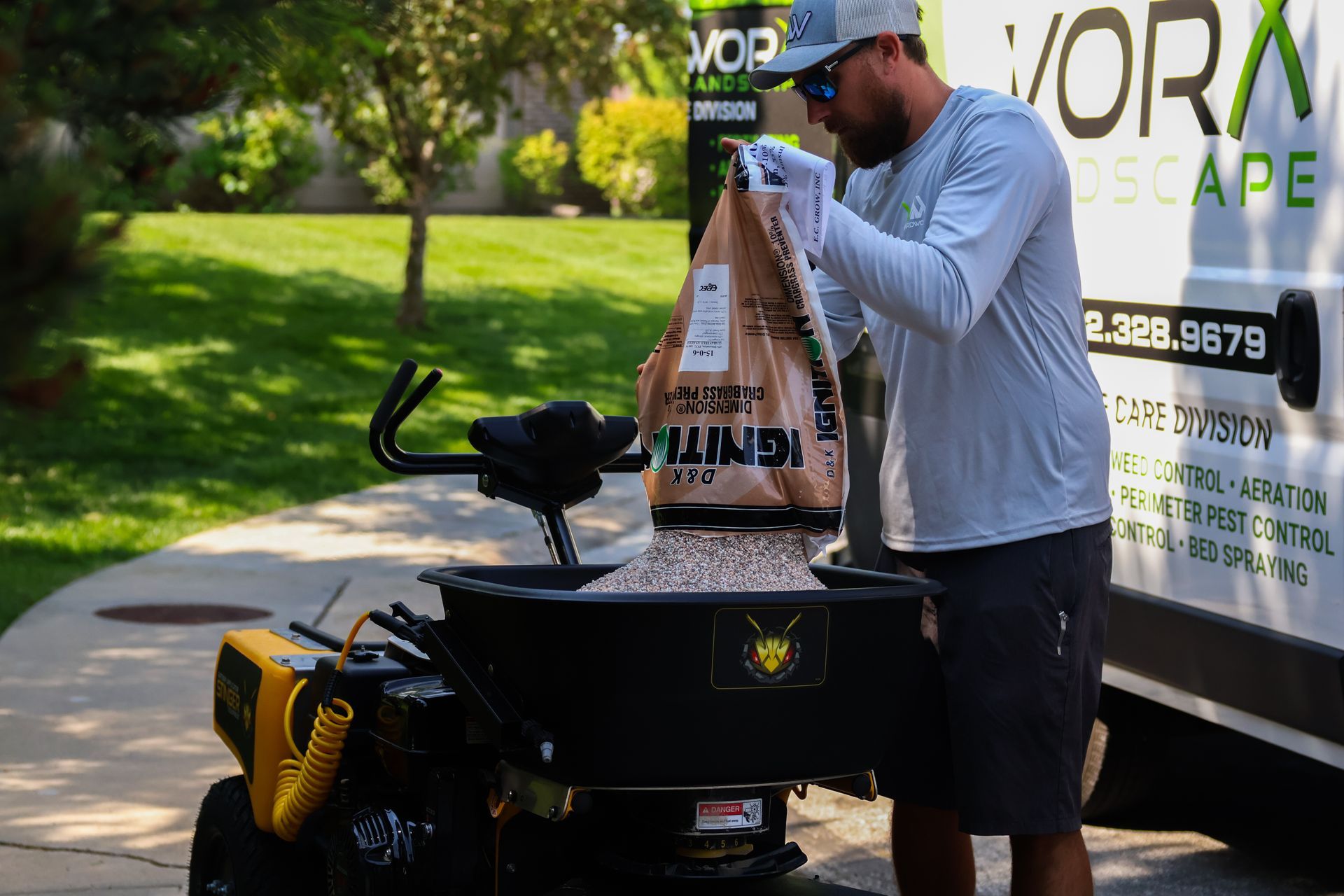 Man filling a lawn spreader with fertilizer near a truck with 
