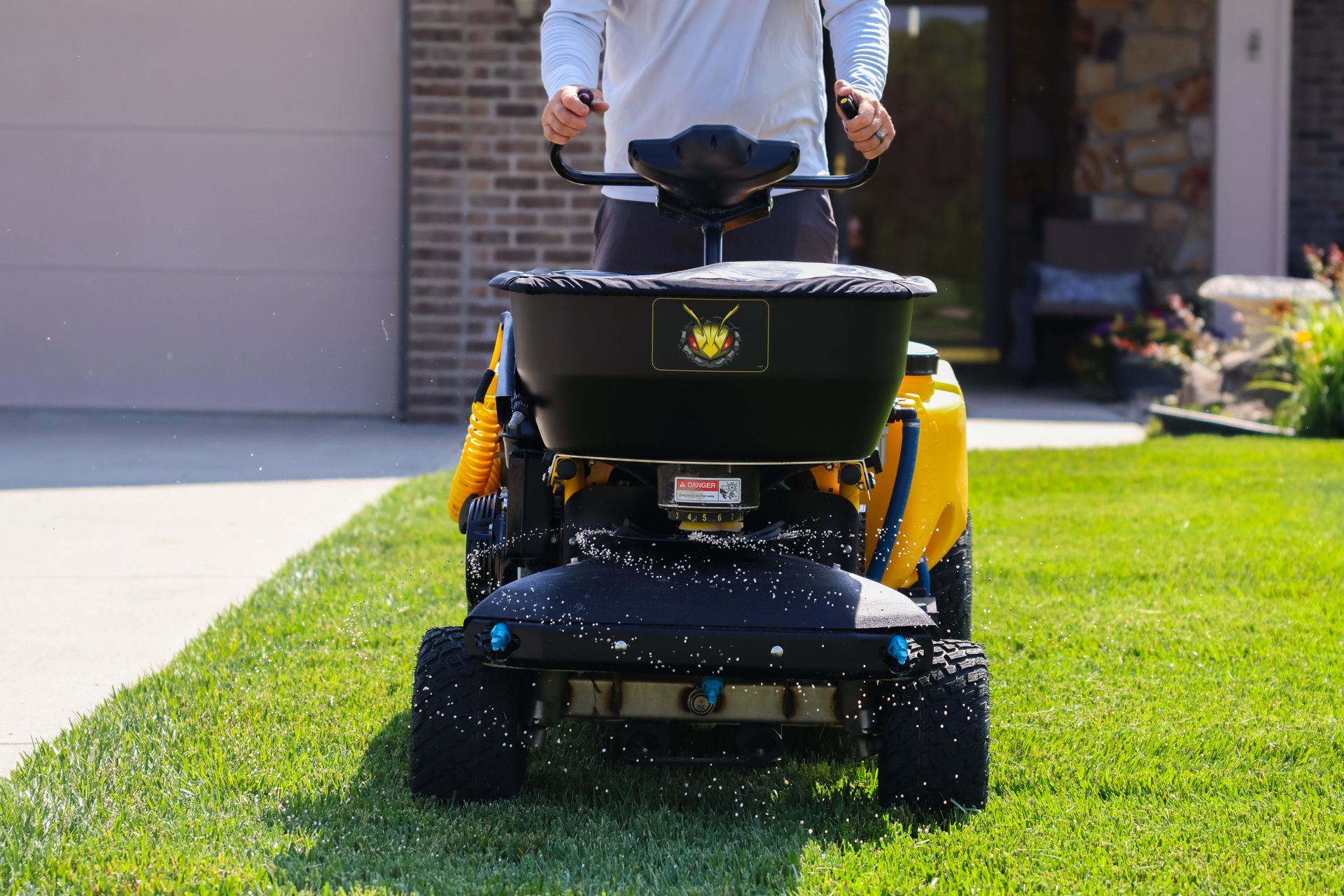 A person operating a yellow spreader on a lawn, dispensing granular product.